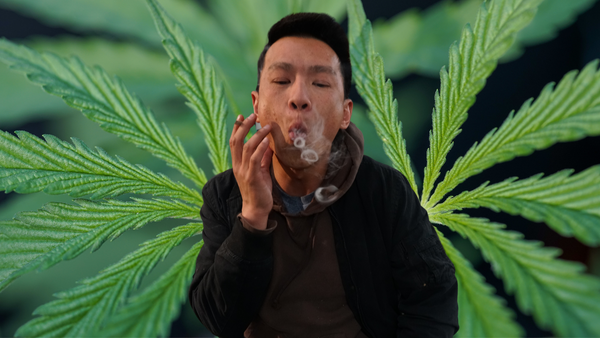 man blowing smoke rings with weed leaves in background
