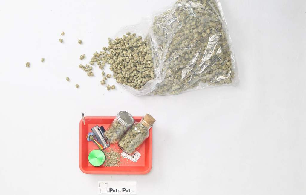 pile of marijuana buds spilling out of a pound bag above a rolling tray with a joint, bowl, grinder, and two ounces of weed