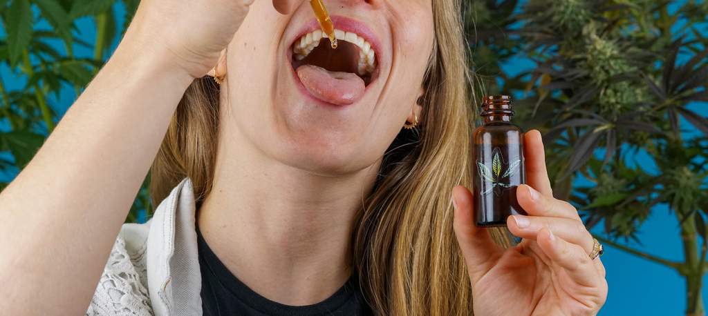 woman consuming cannabis as medicine in the form of a tincture with marijuana plants in the background